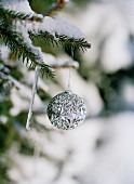 Silberne Weihnachtskugel an schneebedecktem Tannenzweig hängend