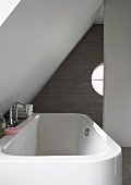 White bathtub under white sloping ceiling