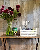 Vintagetisch an Betonwand mit prachtvollem Dahlienstrauss in Glasblumenvase; an der Wand eine Holzbesteck-Collage