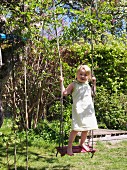 Kleines Mädchen steht auf Schaukel im Garten