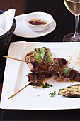Two Skewers of Lamb with Grilled Zucchini and Rice served with a Dipping Sauce and a Glass of White Wine
