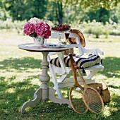 Cherries and hydrangeas on round wooden table and tennis racquets leaning on chair in sunny garden