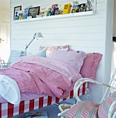 Various red gingham bed linens on bed against white wood-panelled partition wall