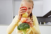 Girl building tower of apples and broccoli