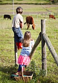 Children next to fence in front of field of cows