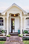 Traditional white wooden house - veranda with turned columns and plant pots on steps leading to half-open front door