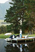 Woman with child and dogs on wooden jetty on lake shore with woods and mountain landscape in background