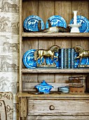 Small, brass horses in front of blue and white plates on shelves of rustic wooden dresser