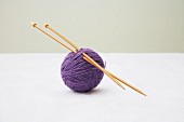 Knitting needles stuck through ball of purple wool