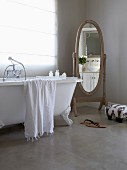 Old-fashioned free-standing mirror and claw foot bathtub standing on polished concrete floor