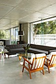 Corner sofa and retro armchairs in open-plan interior of contemporary concrete house