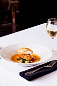 Halibut Served over Greens with a Clam Sauce and Cherry Tomatoes in a White Bowl; Served with a Glass of White Wine