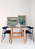 Black chairs, dining table made from wooden trestles and glass top & old paintings decorating wall