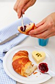 A hand spreading jam on a croissant