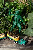 Loaded toy truck on weathered wooden board next to toy soldier in garden