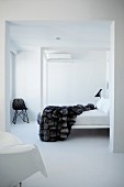 White, minimalist bedroom with fur blanket on canopied bed; Bauhaus wicker chair in corner