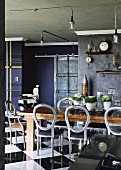 Vintage dining area with antique, Victorian chairs with backrest cushions removed, industrial lamps and dark-painted walls with stucco frieze