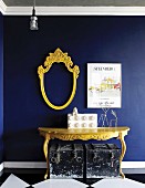 Yellow console table and escutcheon-shaped, empty mirror frame on royal blue wall