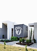 Gravel paths and beds of small conifers in front of unusual detached house incorporating shipping containers