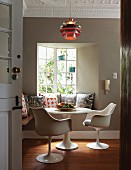 Classic, white swivel chairs and round table in front of bench with many scatter cushions below classic pendant lamp hanging from stucco ceiling