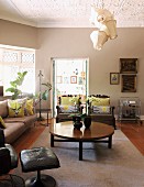 Round coffee table on pale rug and sofa set in elegant living room; whimsical pendant lamp with traditional fabric lampshades hanging from stucco ceiling