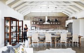 Open-plan interior below white roof beams and brick wall in country-house-style kitchen-dining area with antique furniture