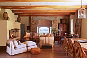 Rustic dining area opposite armchair with matching footstool in front of open fireplace in country-house interior