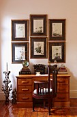 Antique, dark wood chair at desk with drawers below framed pictures on wall