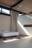 Schlafbereich mit Doppelbett und Kuhfell auf Boden neben Schrank als Raumteiler in zeitgenössischem Wohnhaus mit Oberlicht