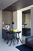 Black breakfast bar and bar stools next to entrance door in modern apartment; mirrored wall enlarges the room