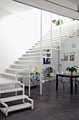 Breiter, luftiger Treppenaufgang in offenem Wohnraum mit Designerstühlen aus Plexiglas und einem schwarzen Esstisch; an der Wand schwarz-weiße Grafik