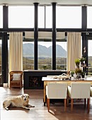 Schwarzer Kaminofen mit zwei Ofenrohren vor prachtvoller Bergkulisse in offenem Wohnraum mit rustikalem Esstisch und weissen Armstühlen
