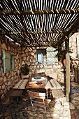 Rustikale Terrasse mit einfachem Sonnenschutz aus langen Bambusstangen und einem Natursteinboden