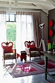 Two armchairs with red and white, polka dotted scatter cushions in front of glass wall and Oriental rug on polished concrete floor
