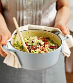A woman holding a casserole pot full of courgette and pea risotto