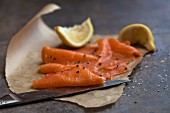 Smoked salmon, lemon wedges and a knife, on grease-proof paper