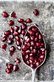 Pomegranate seeds and a spoon on a stone surface