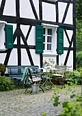 Summery atmosphere on terrace with garden table, garden chairs and bench in front of half-timbered house with green shutters