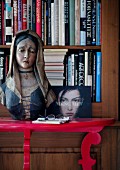 Painted, wooden bust of Madonna on red console table in front of bookcase