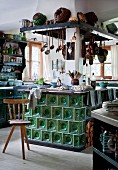 Old tiled stove in centre of rustic kitchen with old kitchen utensils on extractor hood