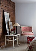 Rustikale Zimmerecke mit Holzwand, davor Beistelltisch mit Tischleuchte und gerahmten Bildern neben Sessel im Rokokostil und rotweiss kariertem Stoffbezug