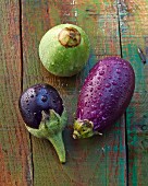 Three assorted baby aubergines on a wooden surface