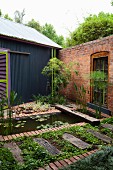 Landscaped pool and beds in courtyard with brick wall adjacent to house with corrugated metal cladding