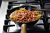 Spaghetti mit Tomatensauce in Pfanne auf dem Gasherd
