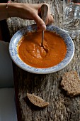 Frauenhand rührt mit Löffel in Kichererbsen-Paprika-Suppe