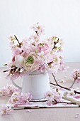 A spring bouquet of ranunculus flowers and ornamental cherry blossom in a tankard vase