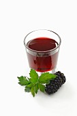 A glass of blackberry syrup, blackberries and blackberry leaves
