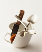 A still life featuring a cup, coffee spoons and ground spice on the end of a knife