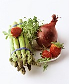 A still life featuring green asparagus, strawberries, an onion and cress