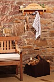 Shelf with hooks upcycled from old wine crate above bench and bag of firewood against rustic stone wall